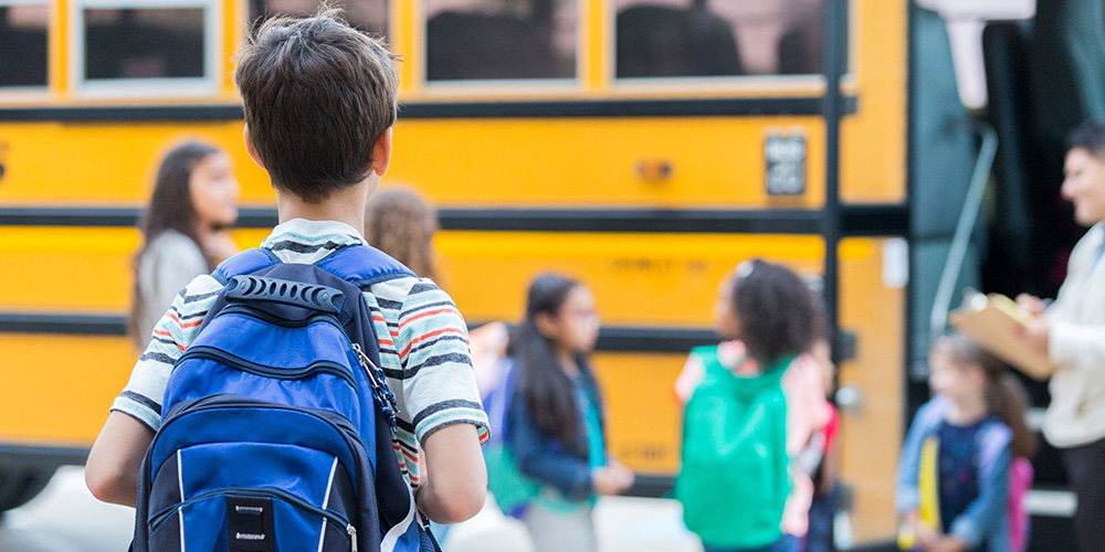 Young boy wearing backpack boards a yellow school bus